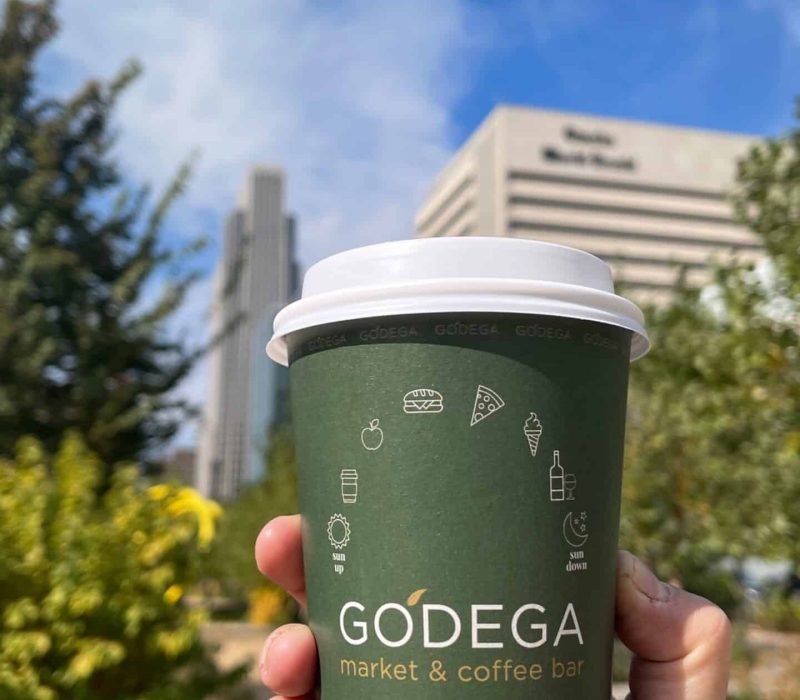 Person holding Godega coffee cup standing outstand of Downtown Omaha, Nebraska